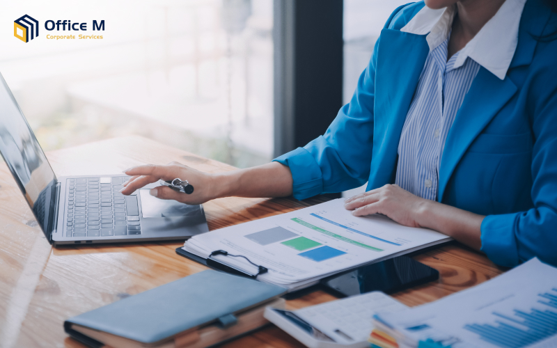 A business professional reviewing data on a laptop and paper.
