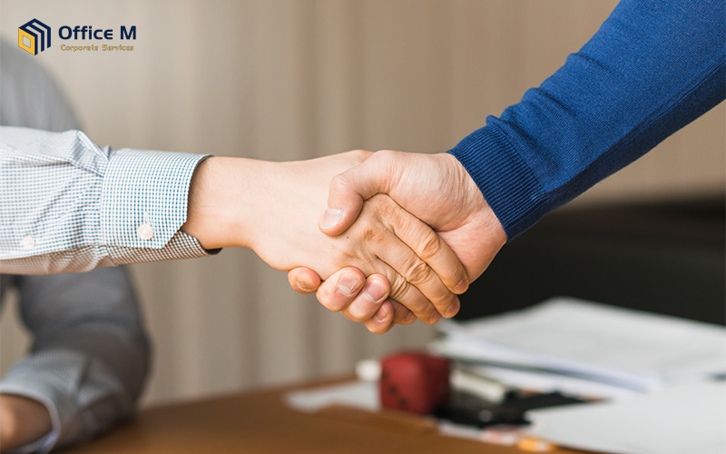 Two people shaking hands across a desk in a professional office setting.